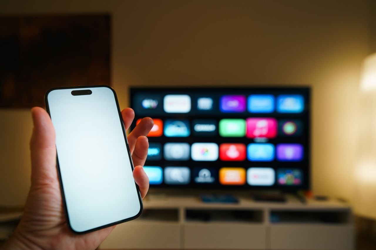 Services A smartphone in focus with a smart TV displaying apps in a cozy living room.