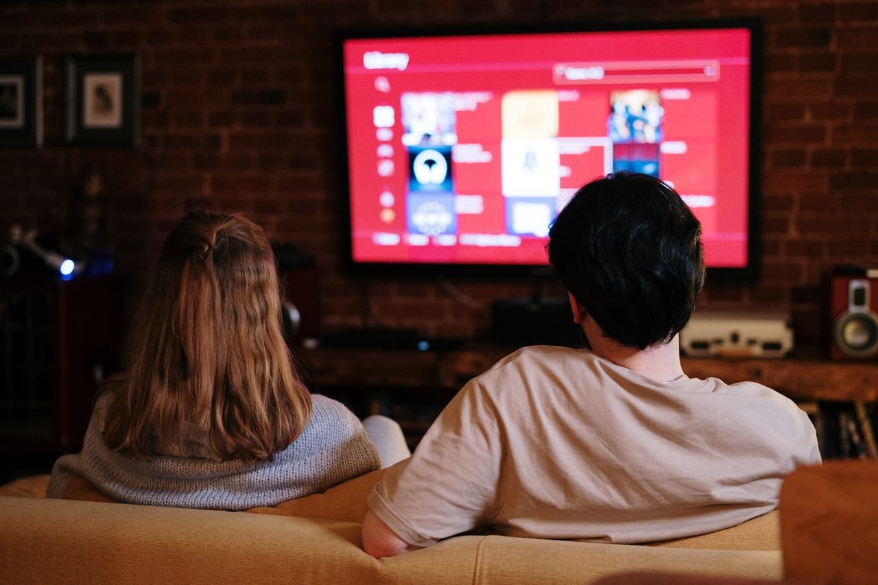 About A couple enjoys streaming shows on a large TV in a cozy, brick-walled living room.